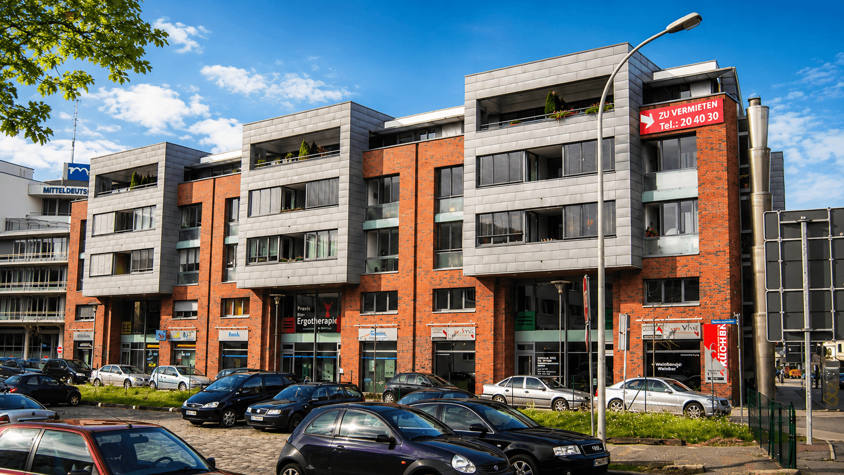 Mehrgeschossiges Gebäude mit Backstein- und Metallfassade an einer belebten Straße.