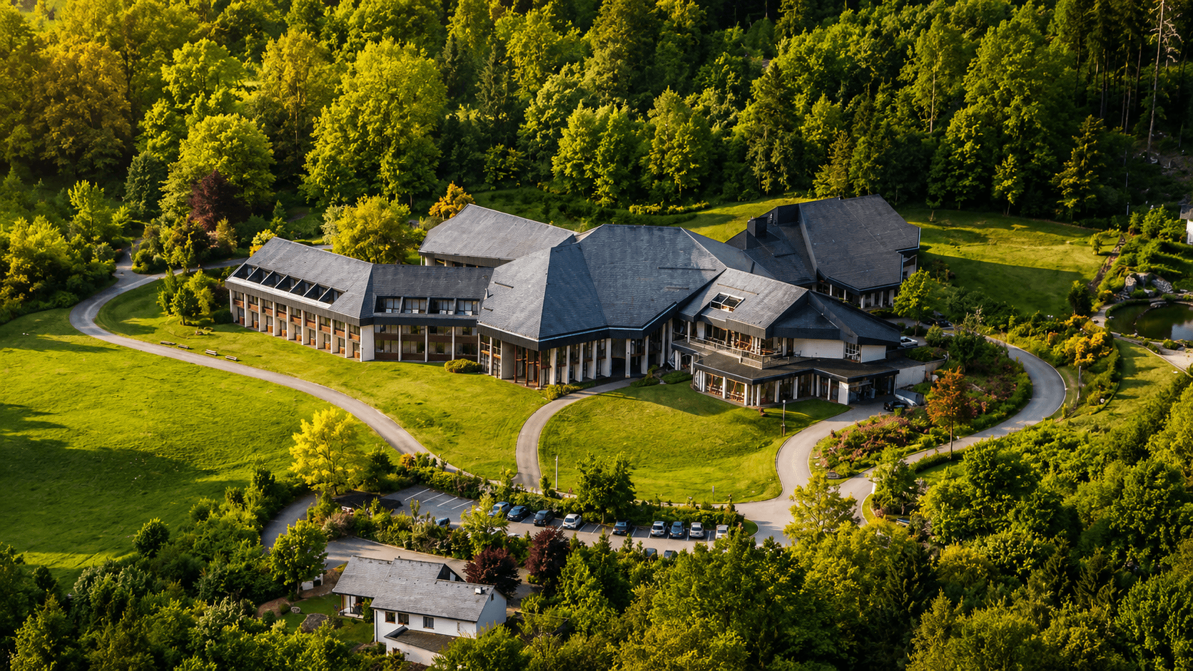 Luftaufnahme eines weitläufigen Gebäudekomplexes in grüner Landschaft.